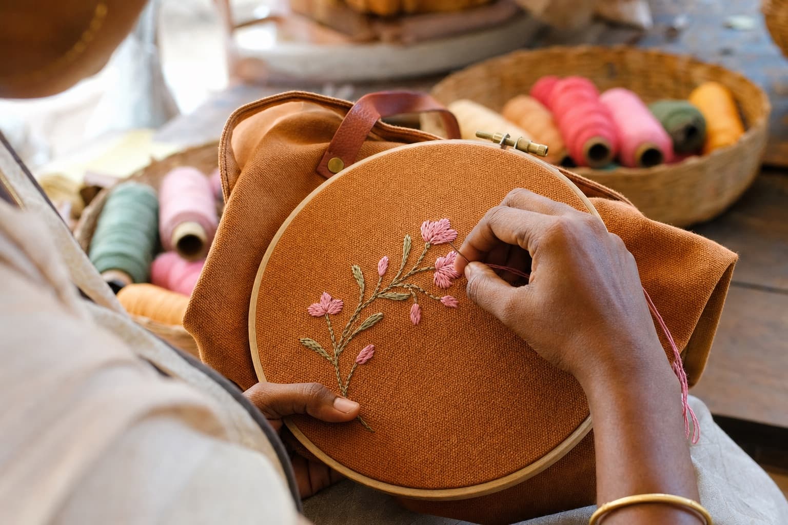 Hand embroidering pink flowers on a canvas bag panel held in an embroidery hoop