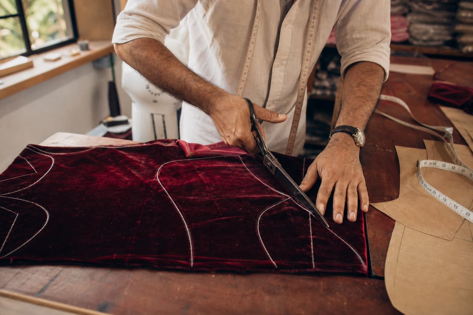 Cutting curved bag panels from burgundy velvet along chalked pattern lines with tailor's shears