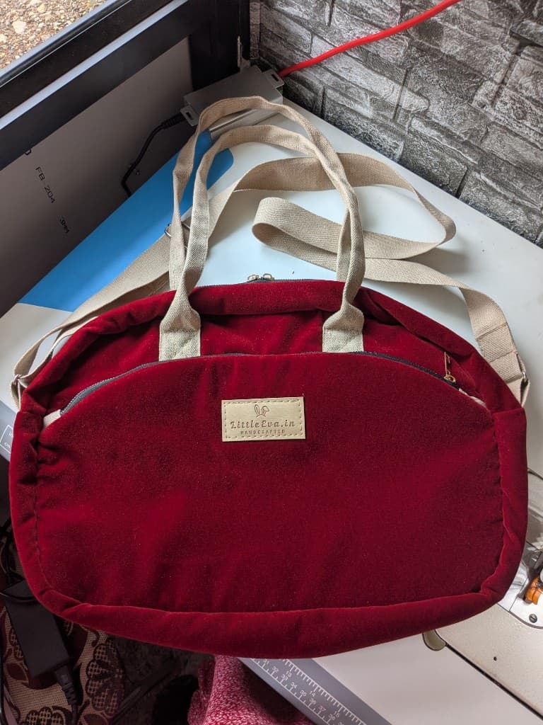Assembled burgundy velvet diaper bag on the sewing table with the LittleEva.in leather label stitched to the front pocket