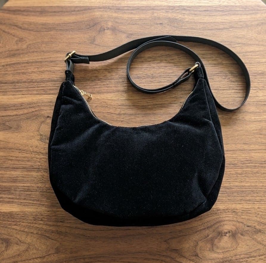 Finished black crescent sling bag with adjustable webbing strap lying on light wood