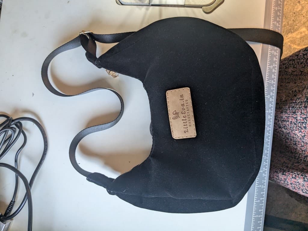 Black sling bag on the worktable with the tan LittleEva.in leather label stitched on the front
