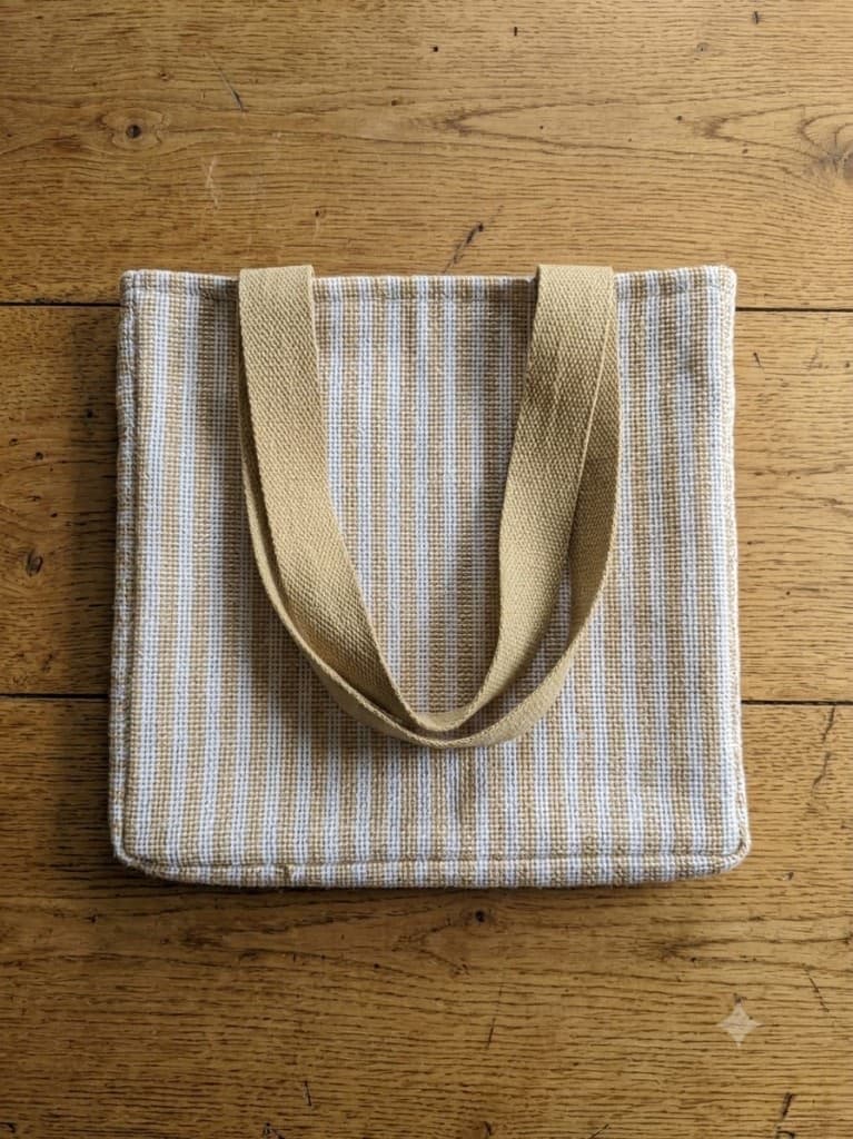 Finished handwoven striped tote bag with tan webbing handles lying on wooden floorboards