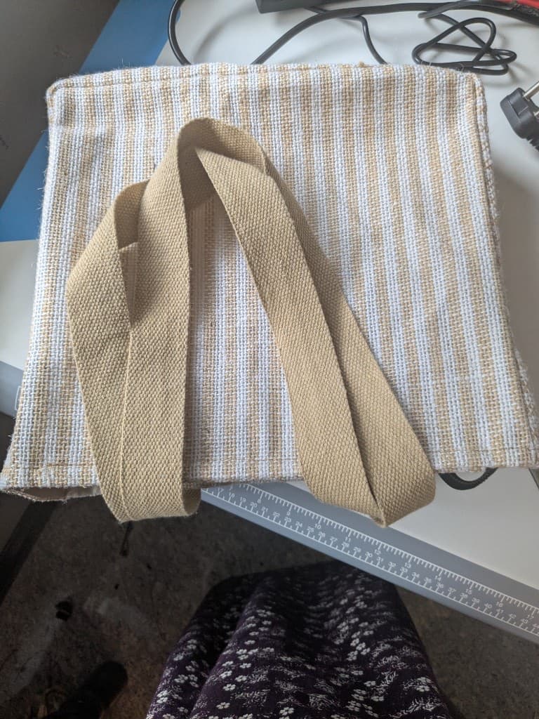 Back of the striped tote on the worktable showing the tan webbing handles stitched to the body