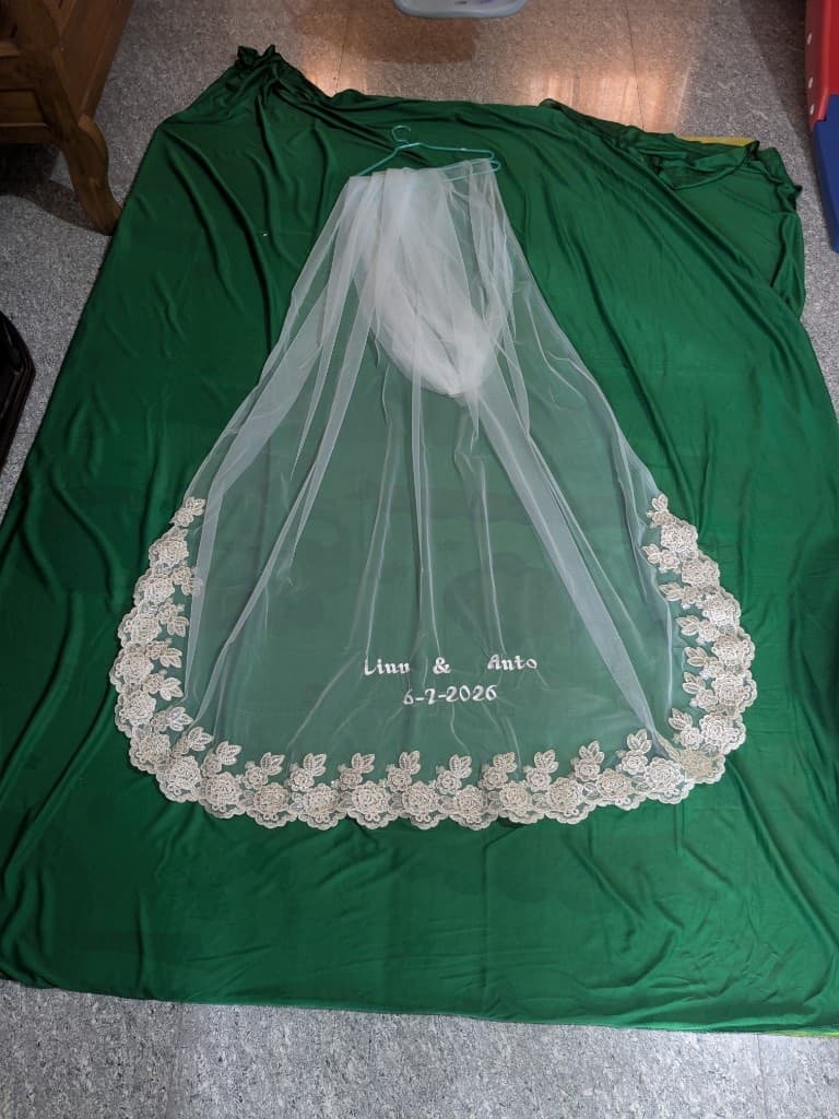 The full veil laid flat on a green backdrop showing the rounded train and lace border taking shape