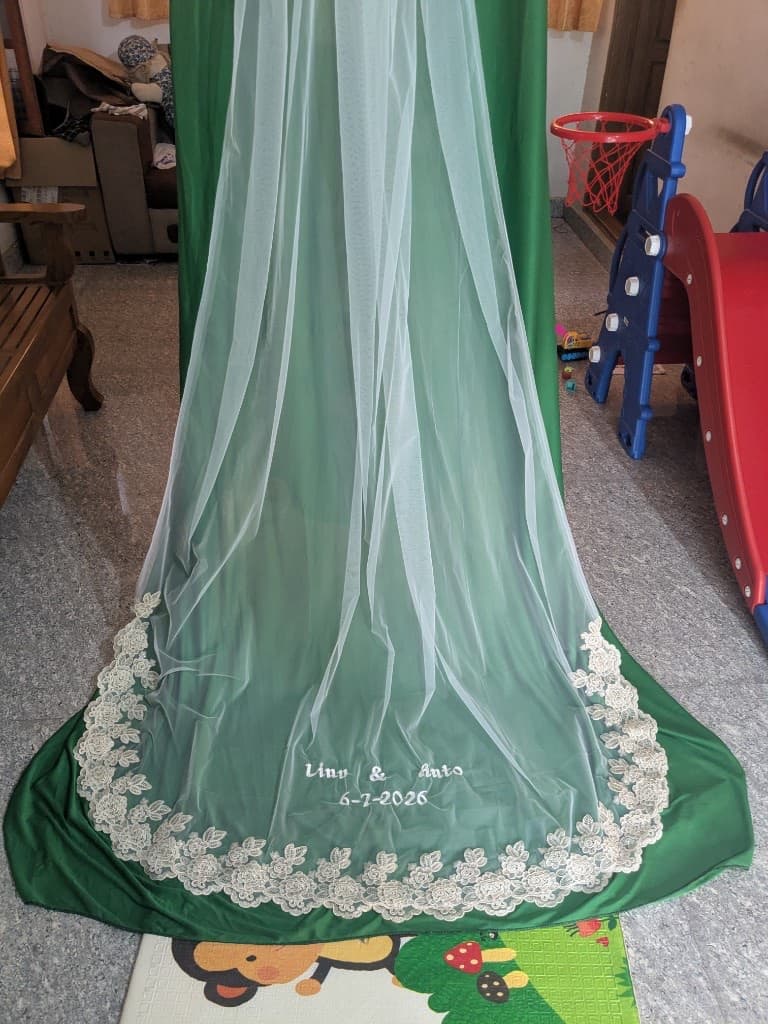 The finished veil hanging full length against a green backdrop, showing the cascade from comb to embroidered train